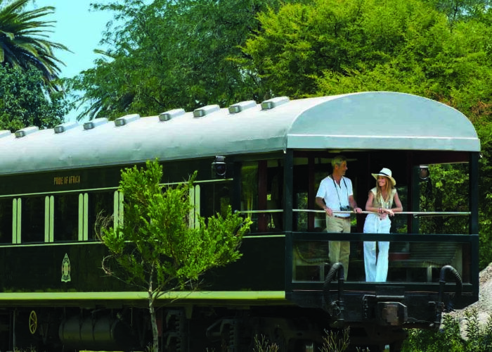 Couple de voyageurs prenant un verre à l'arrière du train de luxe Rovos qui traverse les paysages magnifiques d'Afrique du Sud
